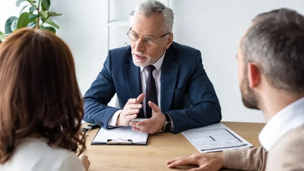 A suited man talks with two persons at a table, indicating a professional discussion